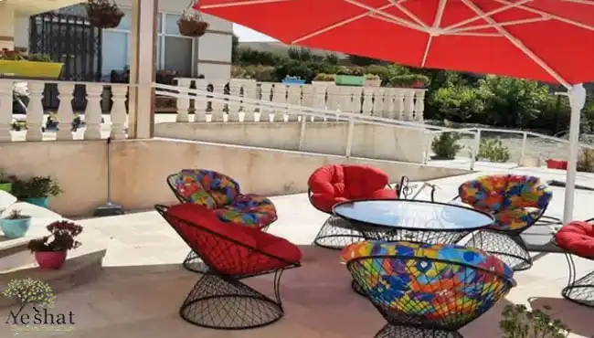 ست صندلی باغی فلزی با تشک‌های رنگارنگ شاد و قرمز، قرار گرفته زیر سایبان قرمز در حیاط گالری نشاط