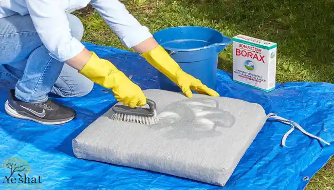 نظافت و شستشوی تشک صندلی باغی خاکستری با برس، دستکش زرد و پودر بوراکس روی زیرانداز آبی - گالری نشاط